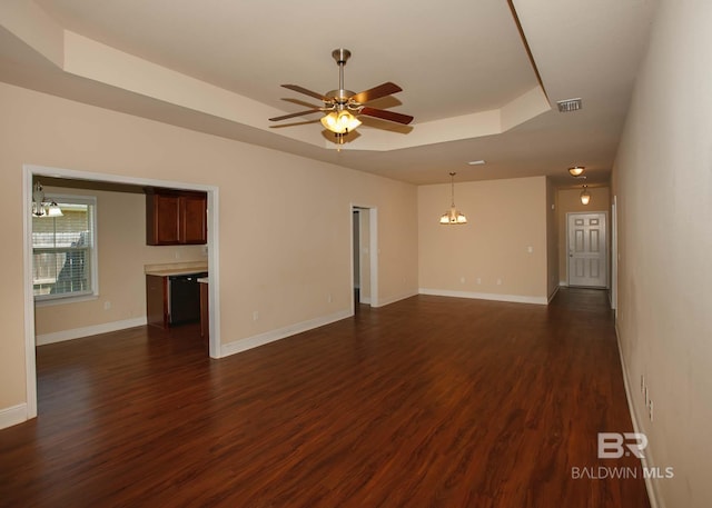 unfurnished living room featuring a tray ceiling, dark wood-type flooring, and ceiling fan with notable chandelier