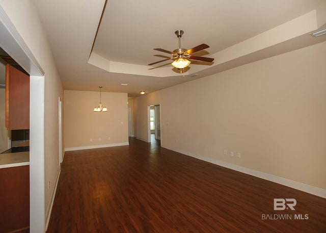 unfurnished room with ceiling fan with notable chandelier, a raised ceiling, and dark wood-type flooring