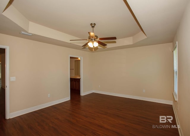 empty room featuring ceiling fan, dark wood-type flooring, and a tray ceiling