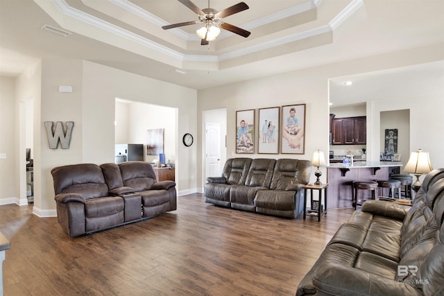 living room with crown molding, visible vents, ceiling fan, dark wood-type flooring, and a tray ceiling