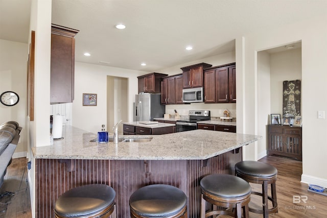 kitchen featuring a kitchen bar, wood finished floors, a sink, a peninsula, and stainless steel appliances