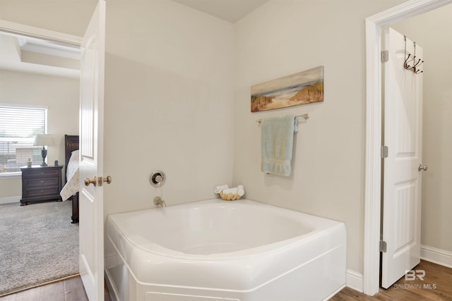 ensuite bathroom with baseboards, ensuite bathroom, wood finished floors, and a garden tub