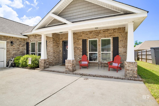 exterior space featuring covered porch, brick siding, and fence