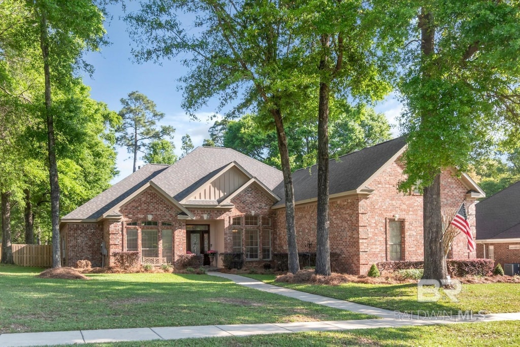 view of front of home with a shingled roof, fence, a front lawn, and brick siding