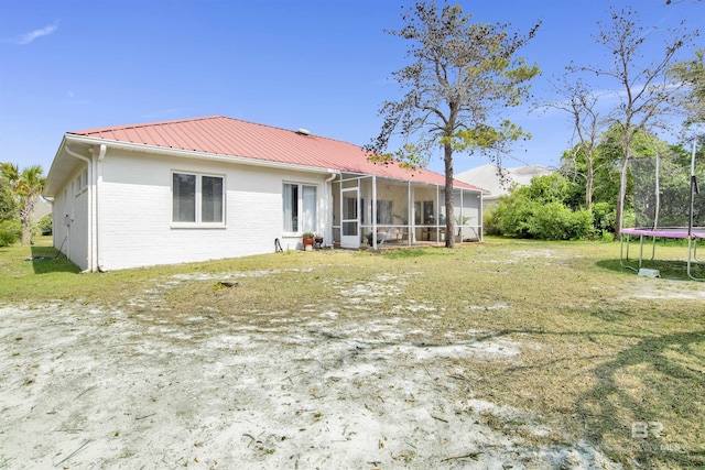 back of house with a lawn, brick siding, metal roof, and a trampoline
