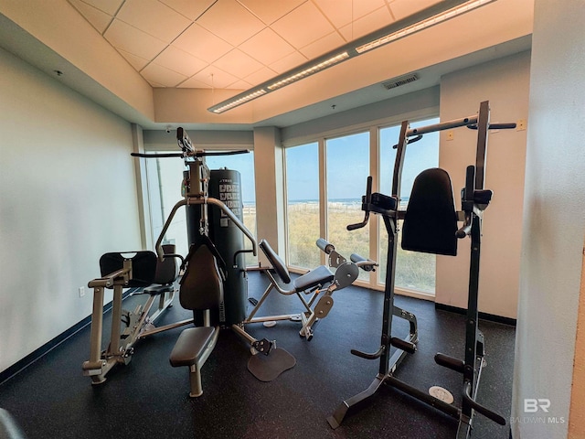 exercise room with a paneled ceiling, a water view, visible vents, and baseboards