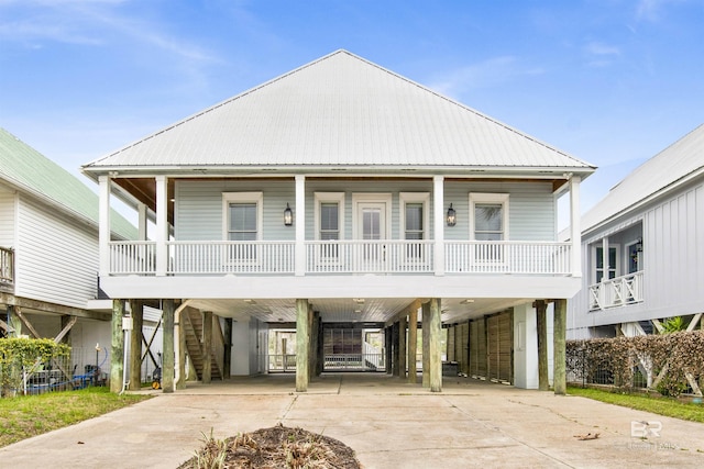 beach home featuring covered porch, concrete driveway, stairway, metal roof, and a carport