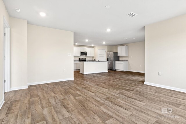 kitchen with white cabinets, a center island with sink, appliances with stainless steel finishes, and light wood-type flooring