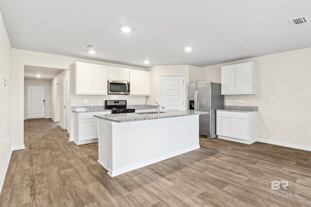 kitchen featuring white cabinets, light stone counters, appliances with stainless steel finishes, and light wood-type flooring