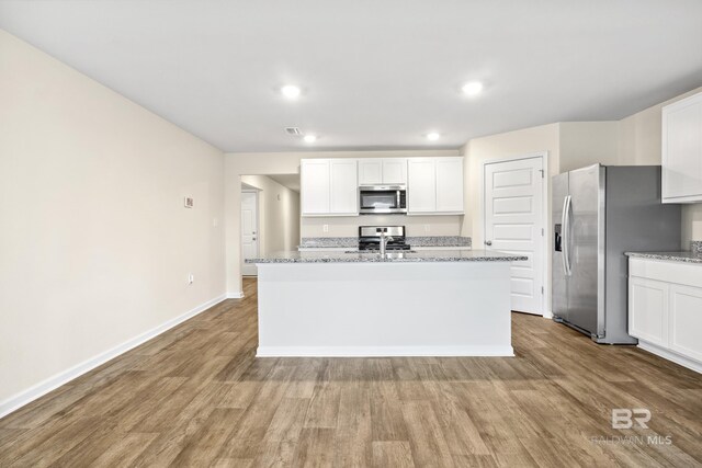 kitchen with an island with sink, dark hardwood / wood-style floors, stainless steel appliances, and white cabinets