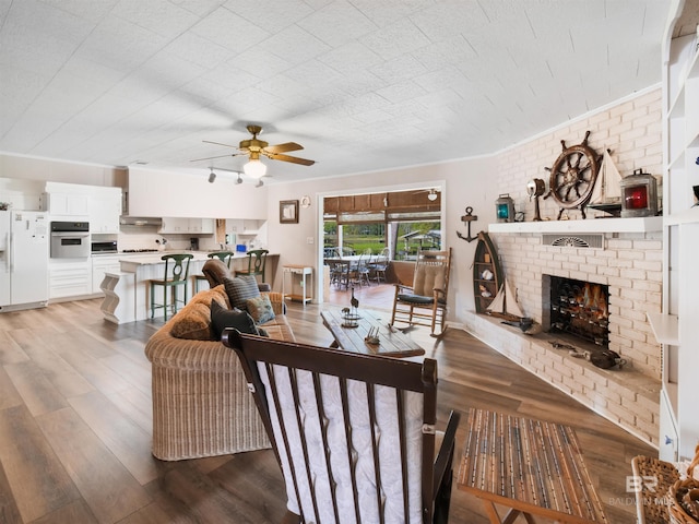 living room featuring ceiling fan, light hardwood / wood-style floors, brick wall, and a brick fireplace