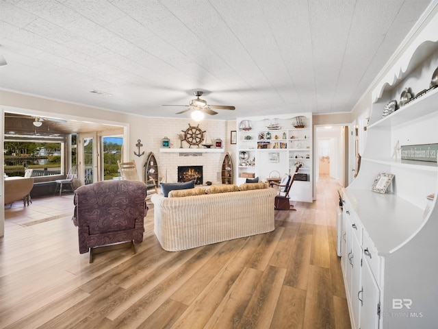 living room featuring hardwood / wood-style floors, ceiling fan, crown molding, and a brick fireplace