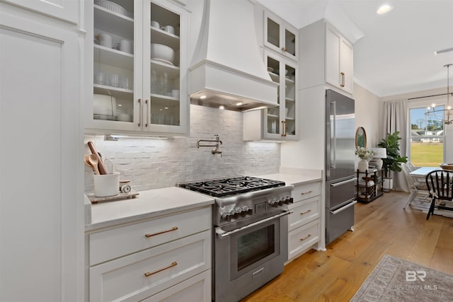 kitchen featuring white cabinetry, premium appliances, light hardwood / wood-style flooring, pendant lighting, and custom range hood