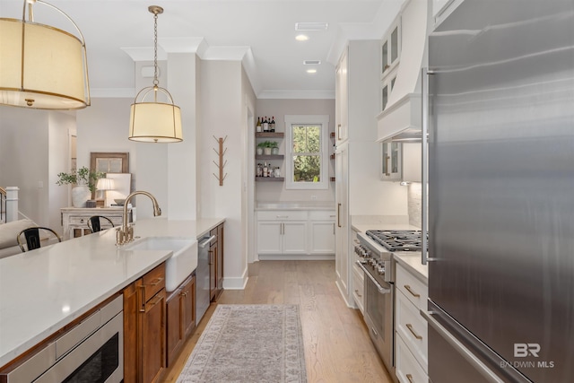 kitchen featuring light wood-type flooring, high end appliances, sink, pendant lighting, and white cabinets