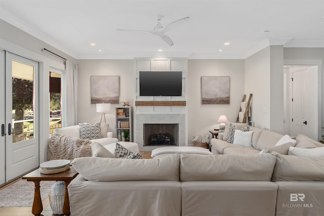 living room featuring a large fireplace, ceiling fan, hardwood / wood-style floors, and crown molding