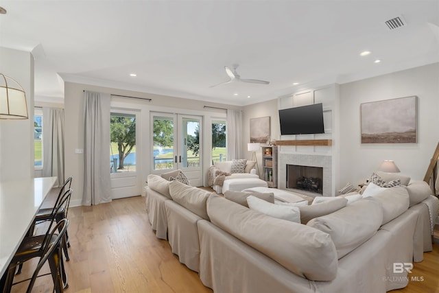 living room with ceiling fan, a large fireplace, french doors, crown molding, and light hardwood / wood-style floors