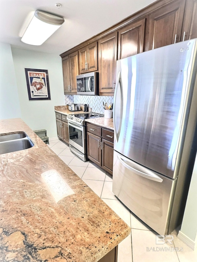 kitchen with dark brown cabinets, light stone countertops, light tile patterned floors, decorative backsplash, and appliances with stainless steel finishes