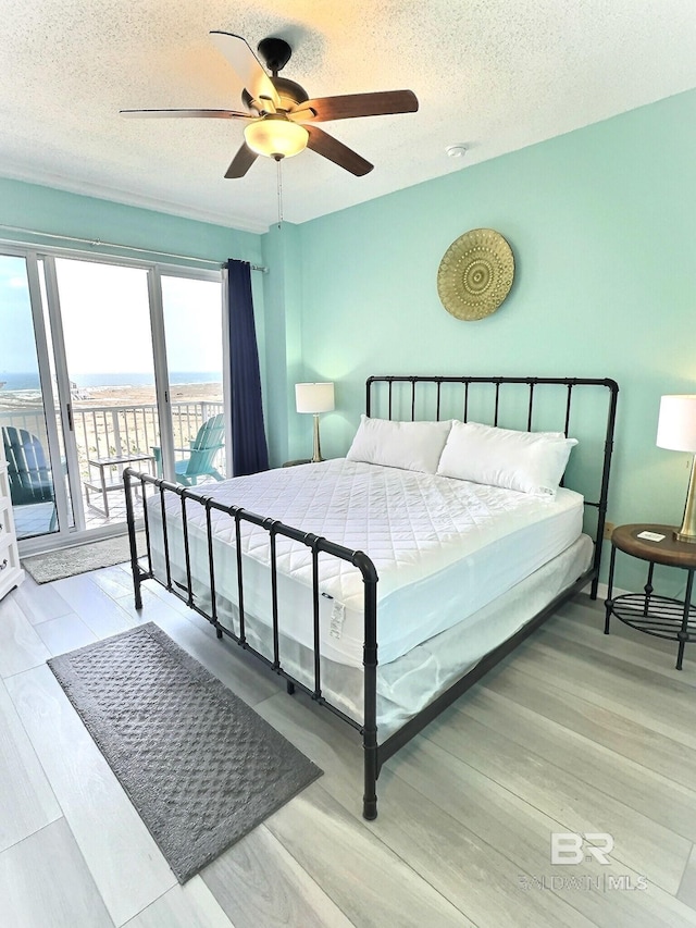 bedroom featuring a ceiling fan, access to exterior, wood finished floors, and a textured ceiling