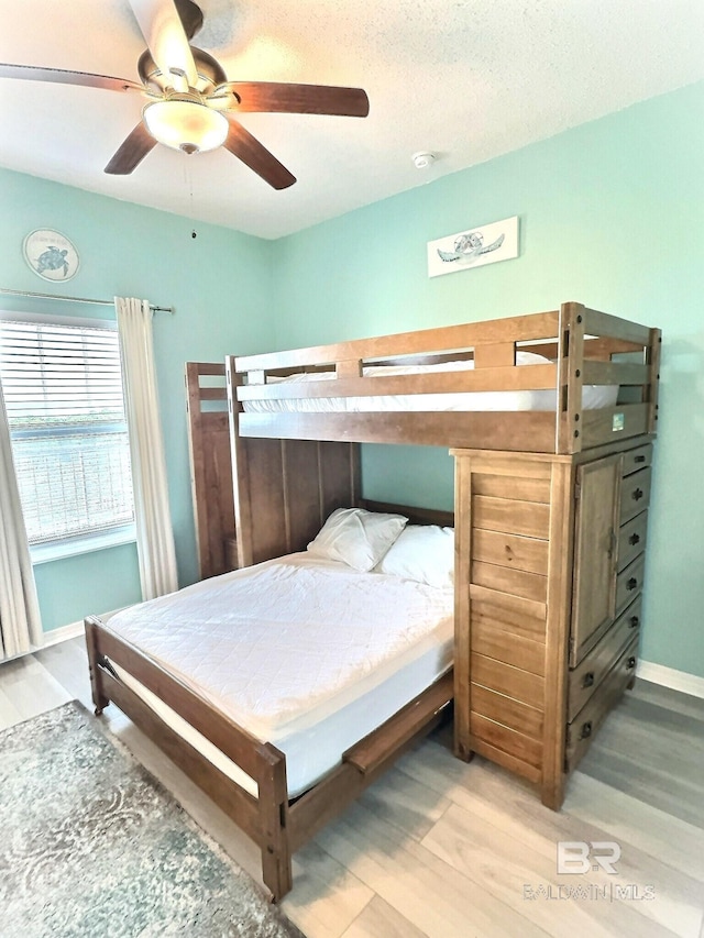 bedroom featuring a textured ceiling, baseboards, light wood finished floors, and ceiling fan