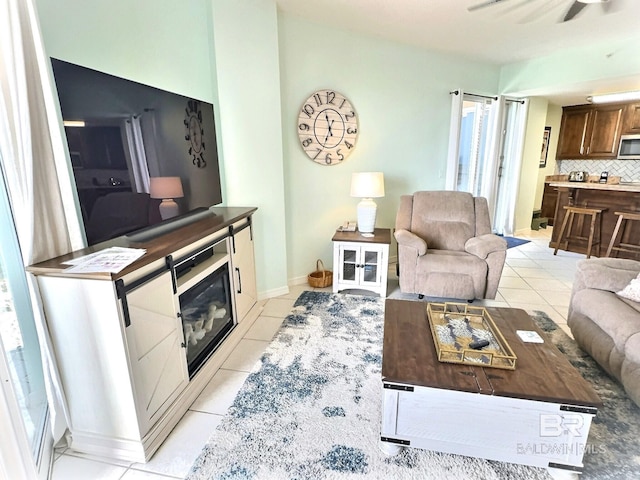 living room featuring ceiling fan, baseboards, a glass covered fireplace, and light tile patterned flooring