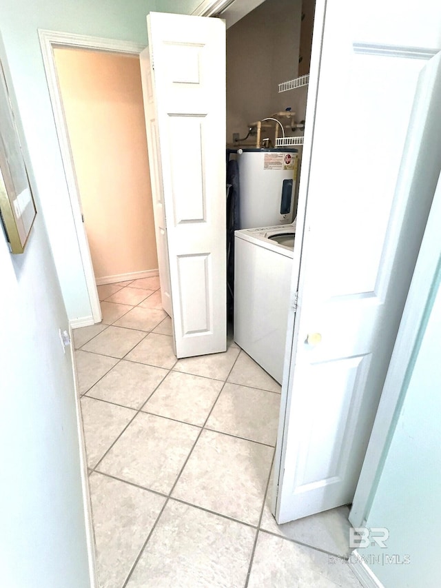 clothes washing area with light tile patterned floors, baseboards, washer / dryer, laundry area, and water heater