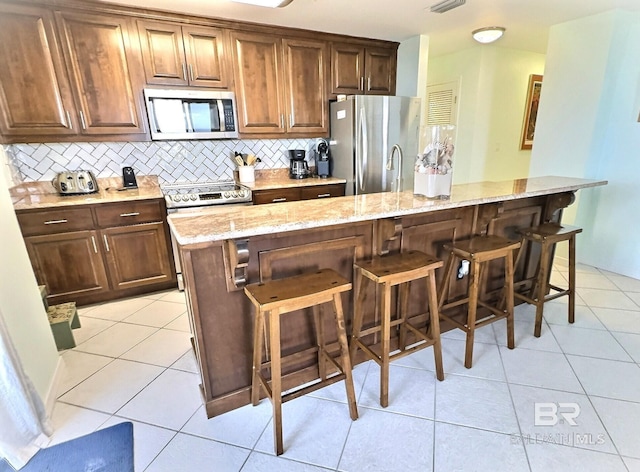 kitchen with light tile patterned floors, stainless steel appliances, and light stone counters