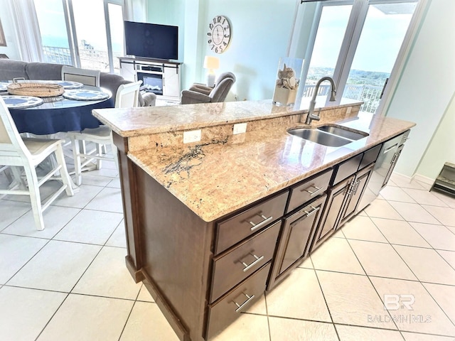 kitchen featuring a sink, light stone countertops, light tile patterned flooring, and a center island with sink