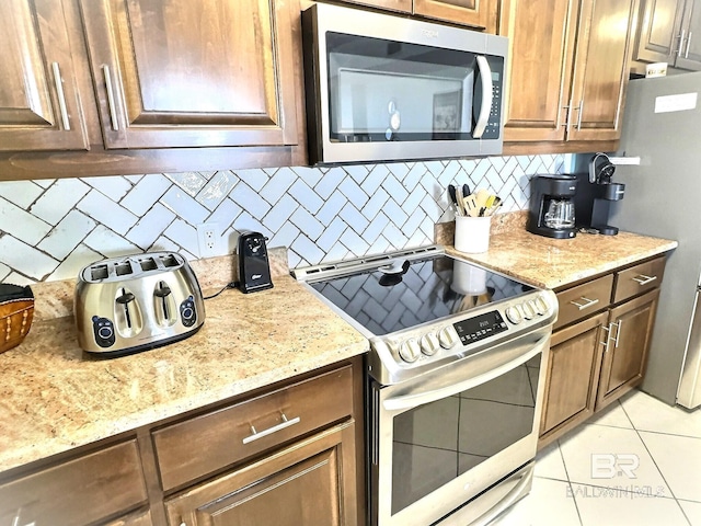 kitchen featuring stainless steel appliances, light stone countertops, tasteful backsplash, and light tile patterned flooring