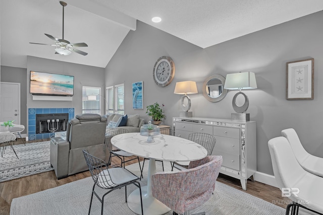 dining area with a fireplace, high vaulted ceiling, a ceiling fan, baseboards, and wood finished floors