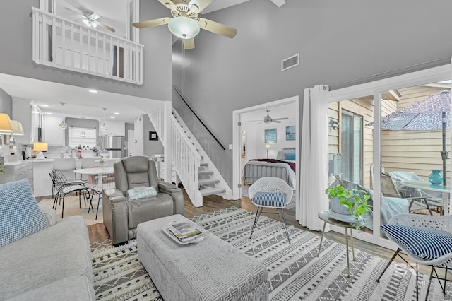 living room featuring ceiling fan, a high ceiling, stairs, wood finished floors, and visible vents