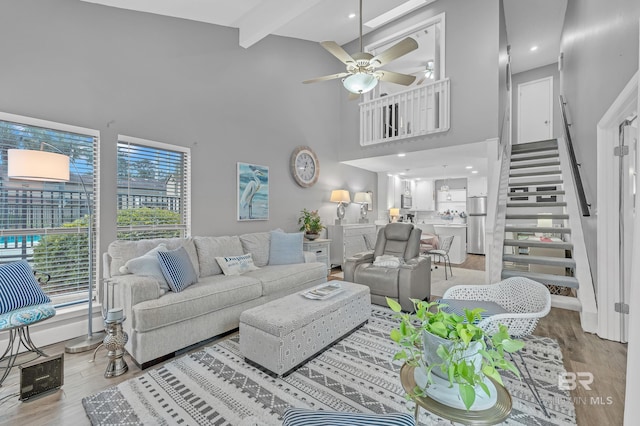 living room featuring a high ceiling, stairs, a ceiling fan, wood finished floors, and beamed ceiling