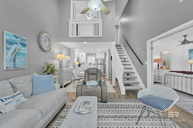 living area with wood finished floors, ceiling fan, a high ceiling, and stairway