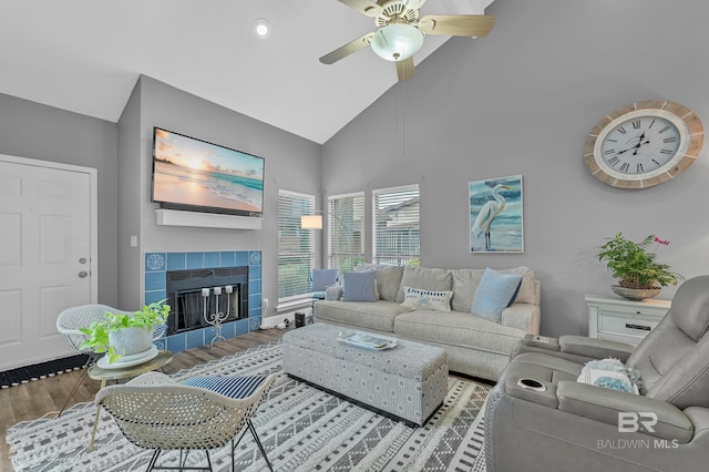 living room featuring a ceiling fan, high vaulted ceiling, wood finished floors, and a tile fireplace