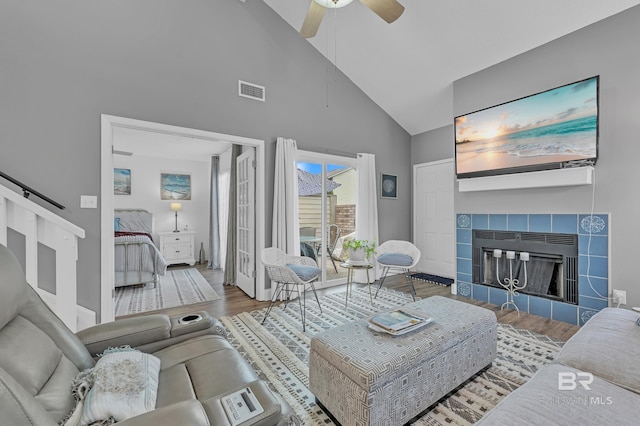 living room featuring wood finished floors, baseboards, ceiling fan, high vaulted ceiling, and a tile fireplace