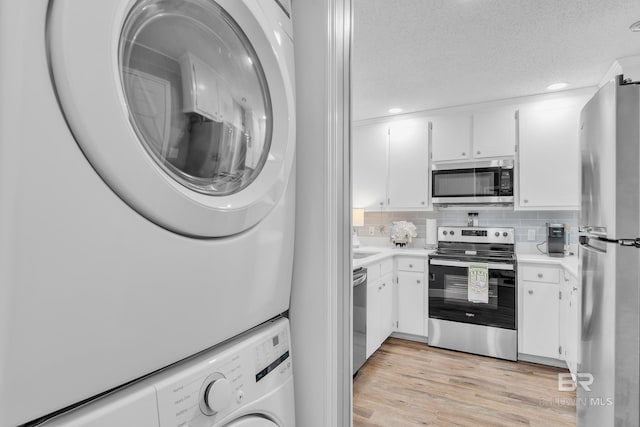 kitchen featuring stacked washer and clothes dryer, light countertops, white cabinetry, light wood-style flooring, and appliances with stainless steel finishes