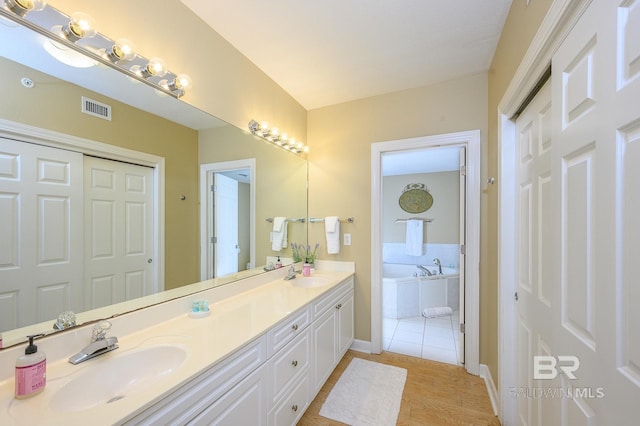 bathroom with hardwood / wood-style floors, a relaxing tiled tub, and vanity