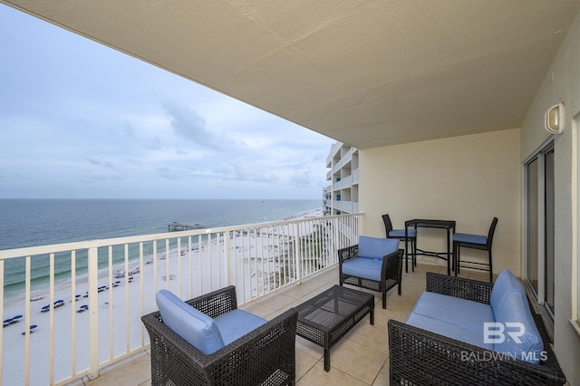 balcony with an outdoor living space, a water view, and a view of the beach