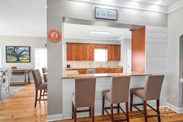 kitchen with light stone counters, light hardwood / wood-style flooring, stainless steel dishwasher, kitchen peninsula, and ornamental molding