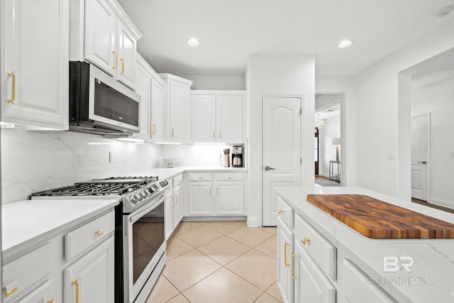 kitchen with white cabinetry, stainless steel appliances, tasteful backsplash, light stone counters, and light tile floors