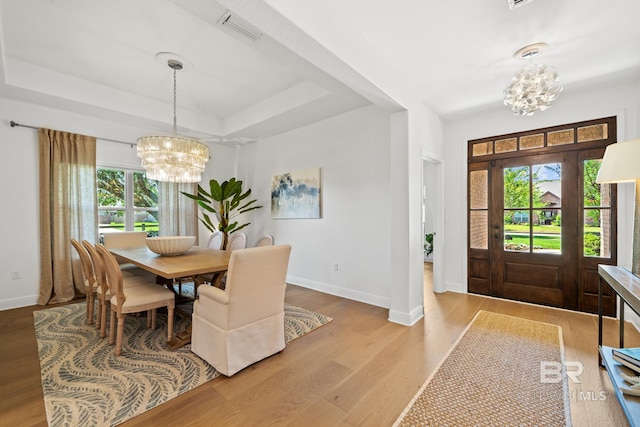 dining area featuring hardwood / wood-style flooring, an inviting chandelier, and a tray ceiling