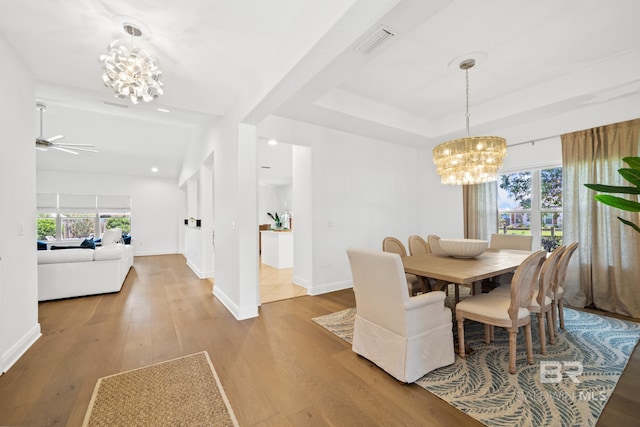 dining area with ceiling fan with notable chandelier, a raised ceiling, and hardwood / wood-style flooring