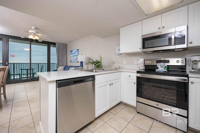 kitchen with appliances with stainless steel finishes, white cabinets, kitchen peninsula, a textured ceiling, and ceiling fan