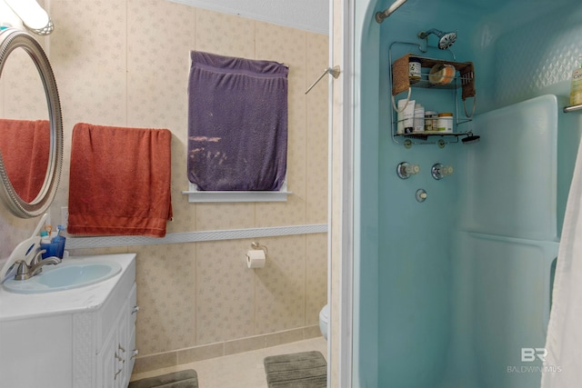 full bath featuring wallpapered walls, toilet, vanity, and walk in shower
