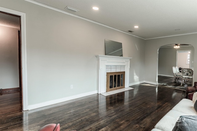 living room featuring ceiling fan, dark wood-type flooring, a fireplace, a textured ceiling, and crown molding