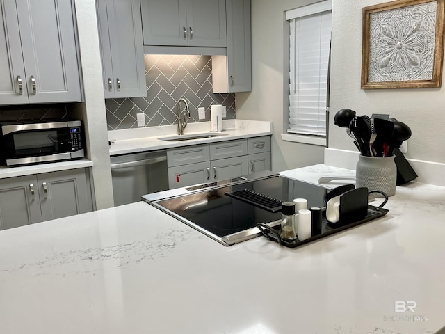 kitchen with a sink, stainless steel appliances, light countertops, gray cabinetry, and backsplash