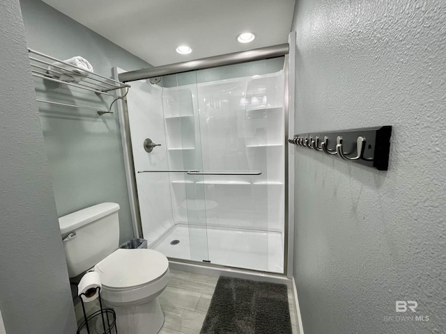 bathroom featuring toilet, a shower stall, and a textured wall