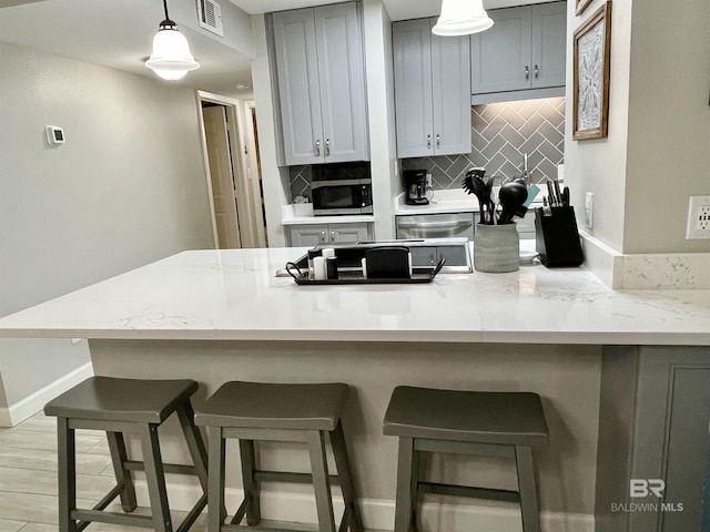 kitchen featuring visible vents, stainless steel microwave, a breakfast bar, pendant lighting, and backsplash