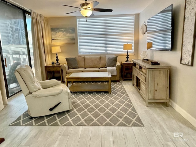 living room featuring a ceiling fan, light wood-type flooring, baseboards, and a wall of windows