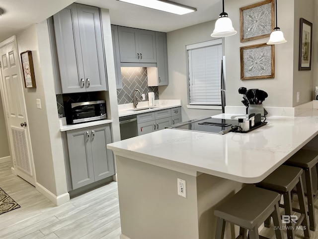 kitchen featuring stainless steel appliances, tasteful backsplash, gray cabinets, a peninsula, and a kitchen breakfast bar