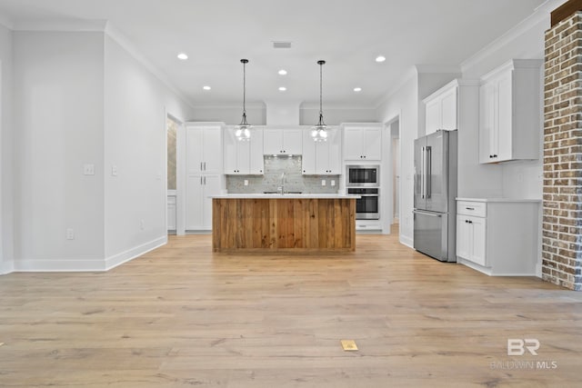 kitchen featuring white cabinets, stainless steel appliances, hanging light fixtures, and a center island with sink